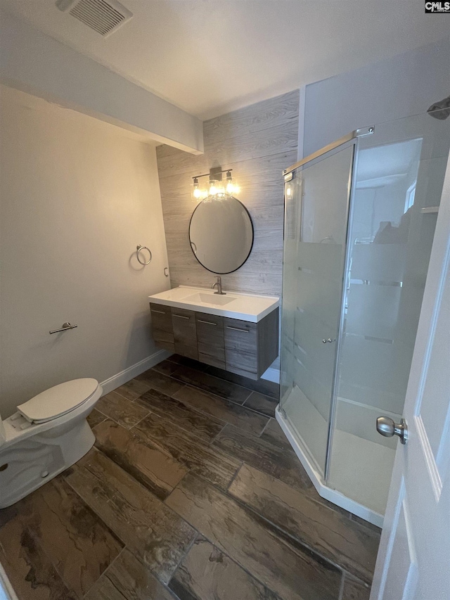 bathroom featuring vanity, a shower with shower door, wooden walls, and toilet