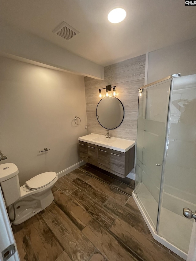 bathroom with toilet, vanity, wooden walls, and a shower with shower door