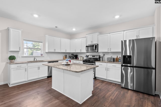 kitchen with dark wood-type flooring, stainless steel appliances, light stone countertops, white cabinets, and a kitchen island