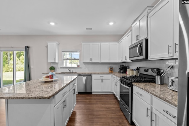 kitchen with white cabinetry, stainless steel appliances, a center island, sink, and light stone counters