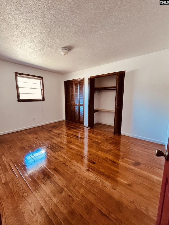 unfurnished bedroom featuring multiple closets, wood-type flooring, and a textured ceiling