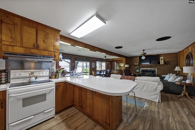 kitchen featuring kitchen peninsula, a brick fireplace, a breakfast bar, electric stove, and ceiling fan