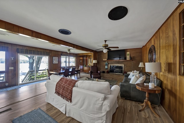 living room featuring a fireplace, hardwood / wood-style flooring, wooden walls, and ceiling fan