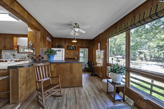 kitchen featuring white refrigerator, ceiling fan, kitchen peninsula, hardwood / wood-style flooring, and wooden walls