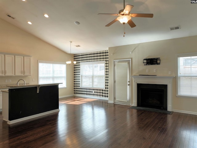 unfurnished living room with ceiling fan with notable chandelier, vaulted ceiling, and dark wood-type flooring