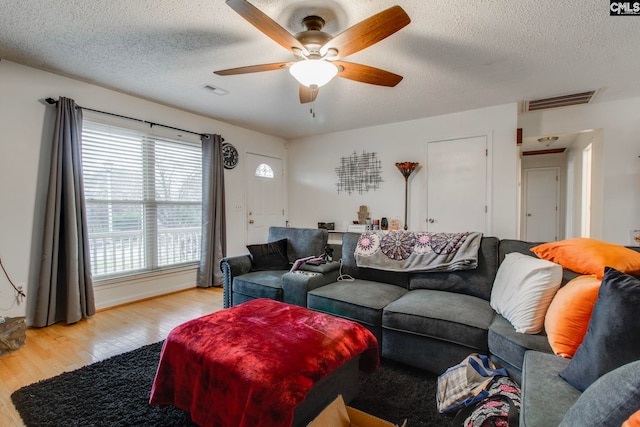 living room with ceiling fan, light wood-type flooring, and a textured ceiling