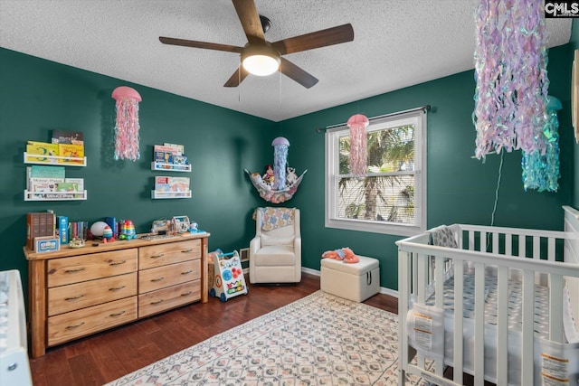 bedroom with a textured ceiling, dark wood-type flooring, ceiling fan, and a nursery area