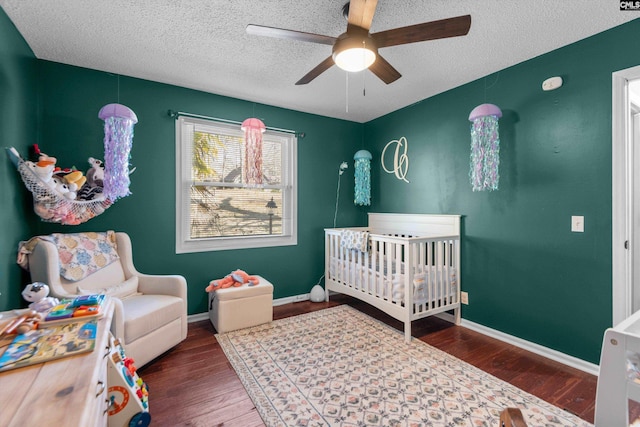 bedroom with a crib, hardwood / wood-style flooring, a textured ceiling, and ceiling fan