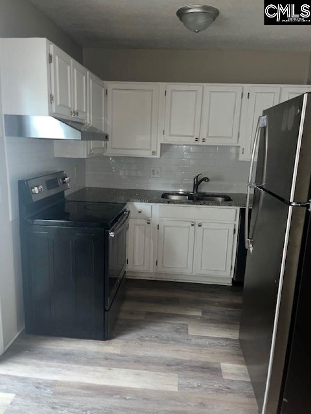 kitchen with sink, backsplash, white cabinetry, stainless steel refrigerator, and black / electric stove