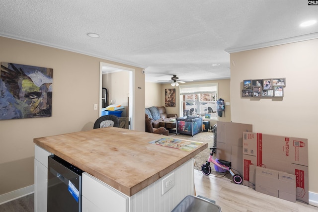 kitchen featuring a textured ceiling, light hardwood / wood-style floors, crown molding, butcher block countertops, and white cabinets