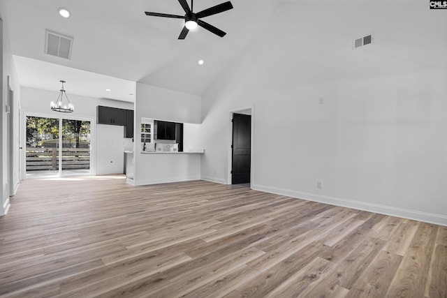 unfurnished living room featuring ceiling fan with notable chandelier, high vaulted ceiling, and wood-type flooring