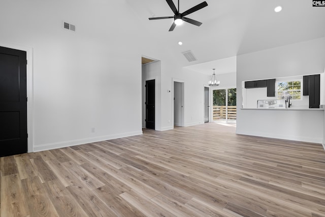 unfurnished living room with ceiling fan with notable chandelier, light wood-type flooring, and high vaulted ceiling