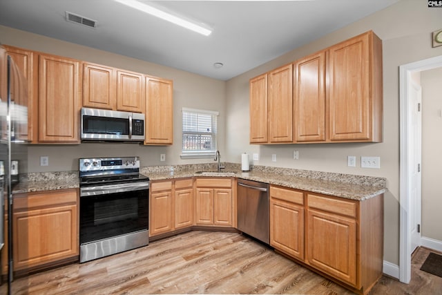 kitchen featuring sink, appliances with stainless steel finishes, light wood-type flooring, and light stone countertops