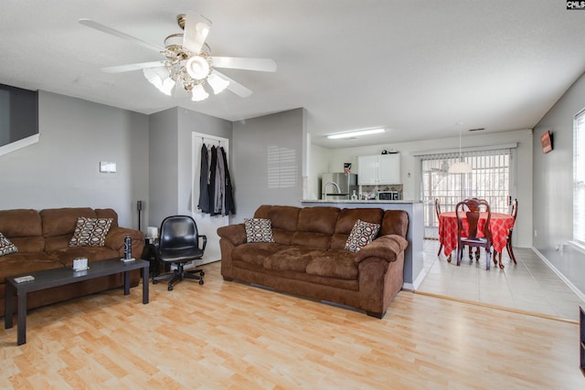 living room with light wood-type flooring, ceiling fan, and a textured ceiling