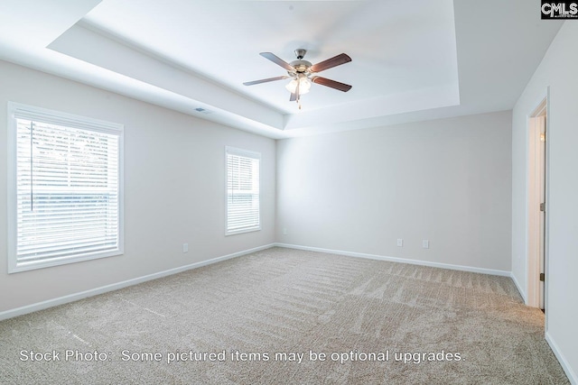 carpeted spare room with a raised ceiling and ceiling fan