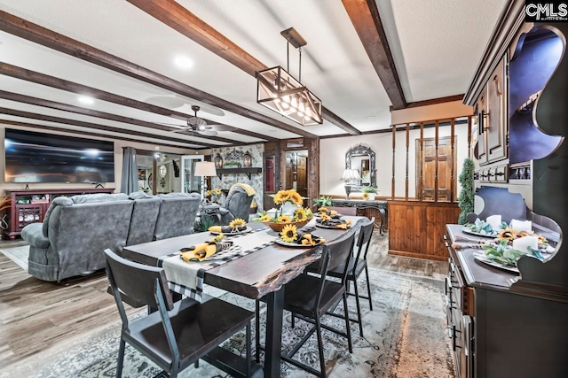 dining area featuring light hardwood / wood-style floors, beamed ceiling, a stone fireplace, and ceiling fan