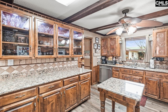 kitchen with light wood-type flooring, beam ceiling, light stone countertops, sink, and stainless steel dishwasher