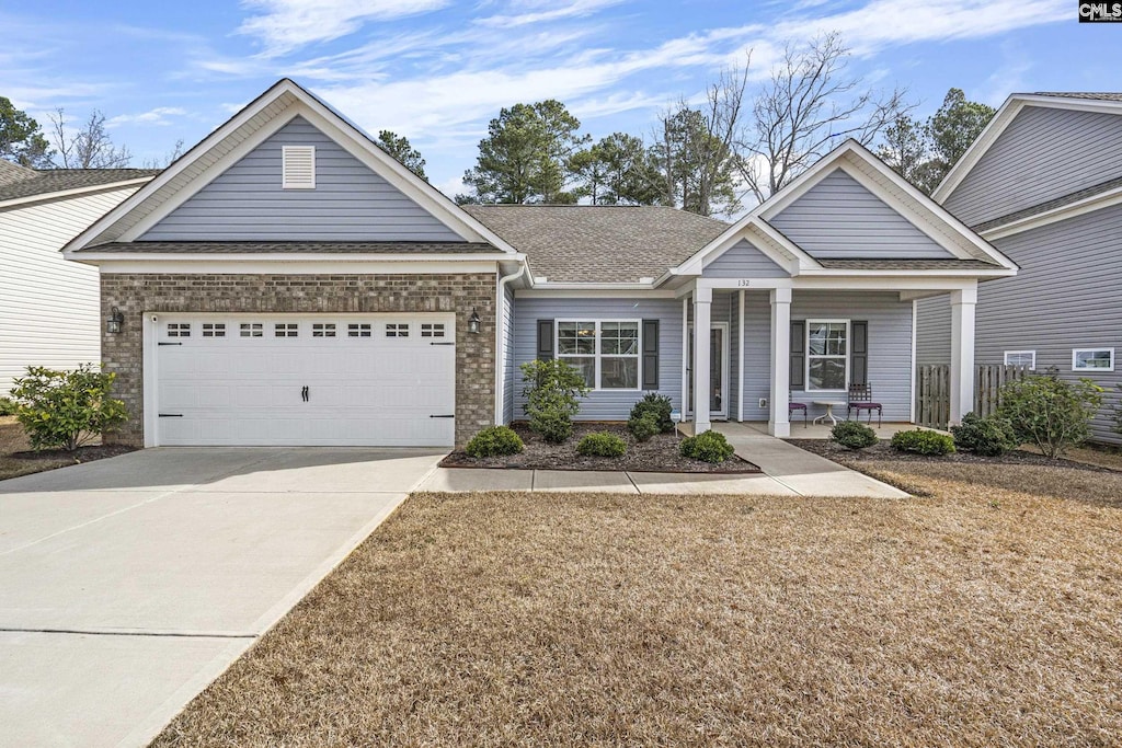 view of front of property featuring covered porch, a garage, and a front lawn