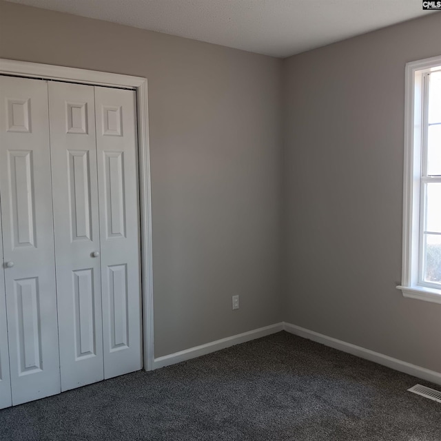 unfurnished bedroom with dark carpet and a closet