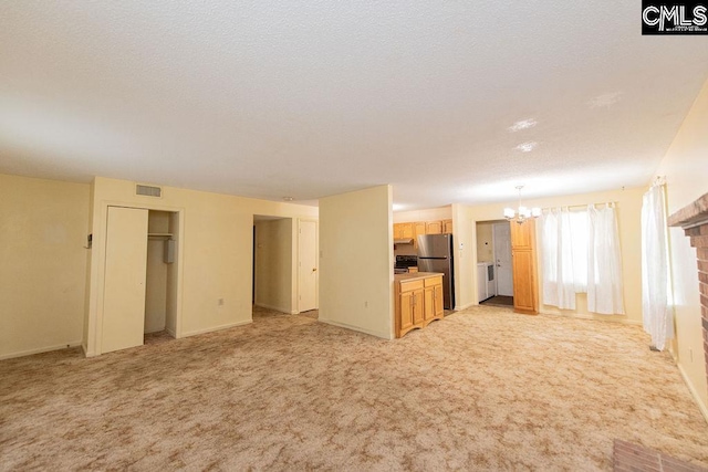 unfurnished living room featuring a chandelier, a textured ceiling, visible vents, and light colored carpet