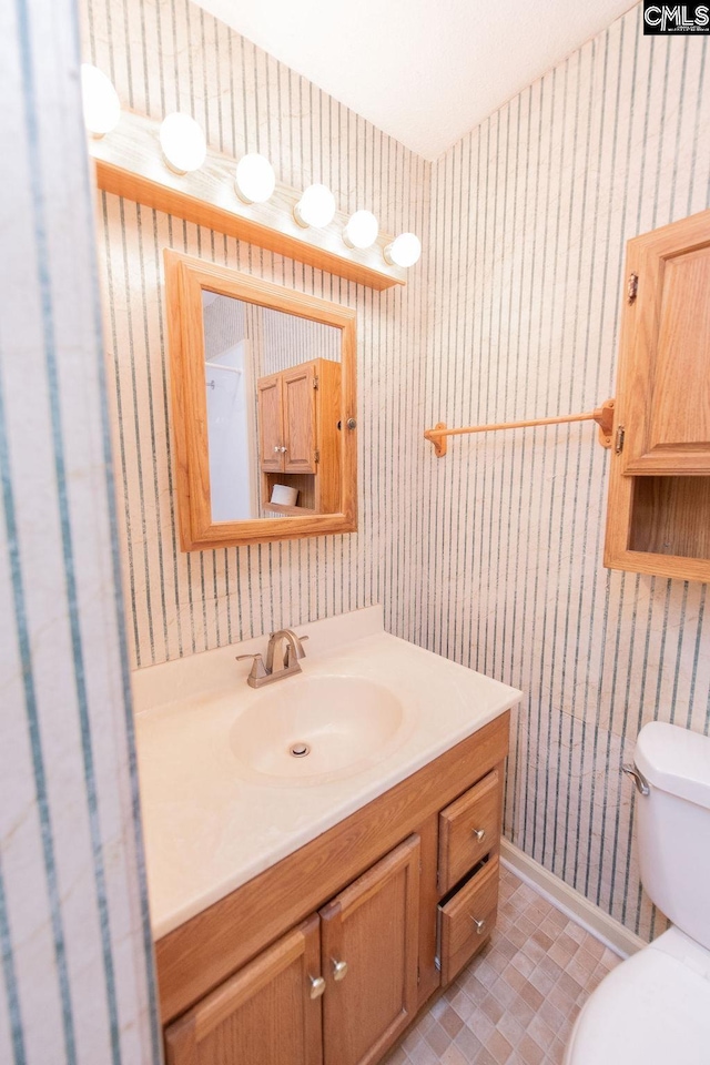 bathroom with baseboards, vanity, toilet, and wallpapered walls