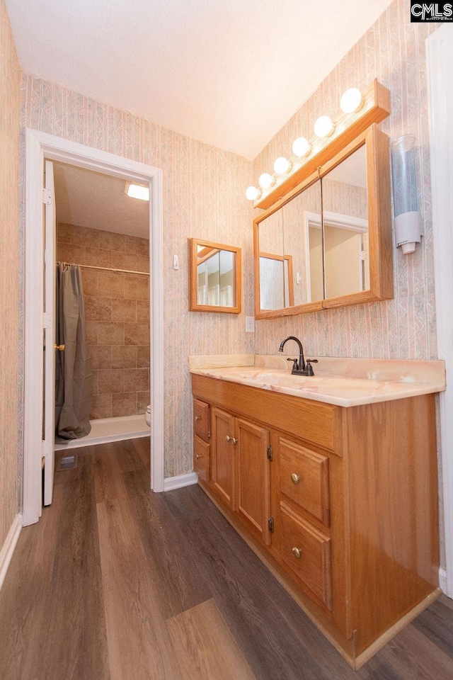 bathroom featuring wood finished floors, vanity, baseboards, a stall shower, and wallpapered walls