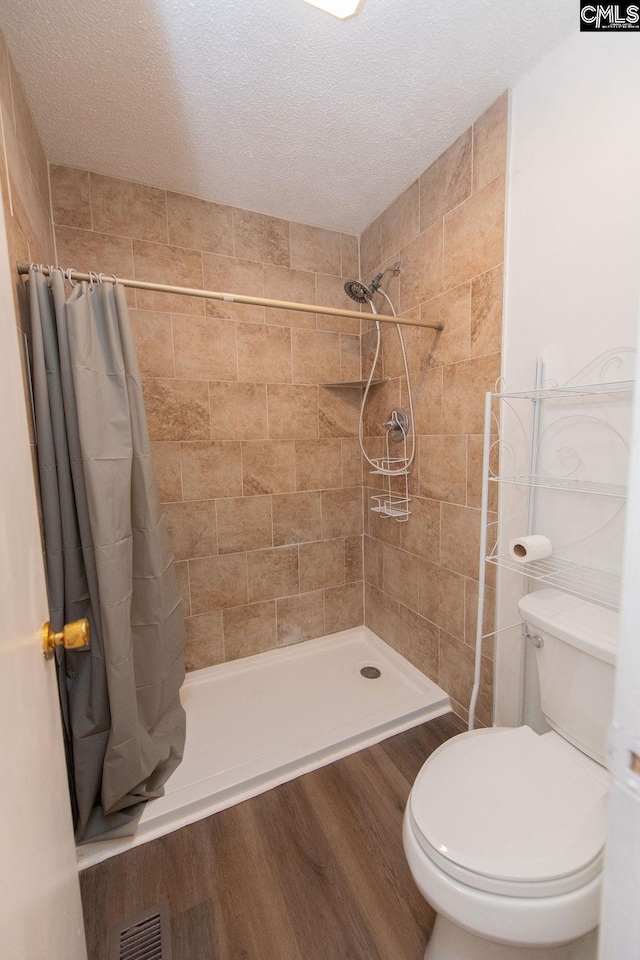 bathroom featuring wood finished floors, visible vents, toilet, and tiled shower