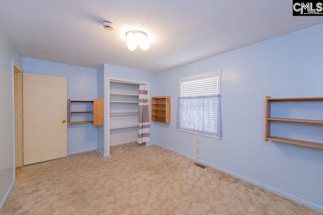 unfurnished bedroom featuring a closet, light colored carpet, visible vents, a textured ceiling, and baseboards