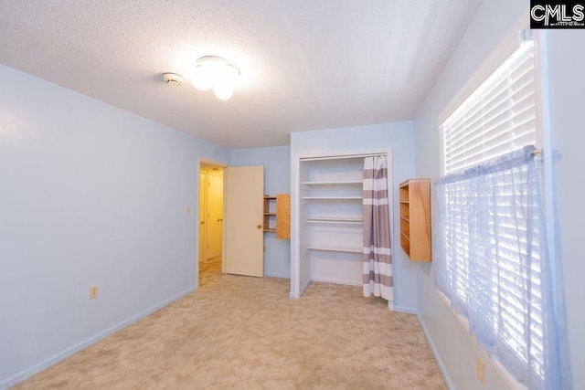 unfurnished bedroom featuring a textured ceiling, a closet, baseboards, and light colored carpet