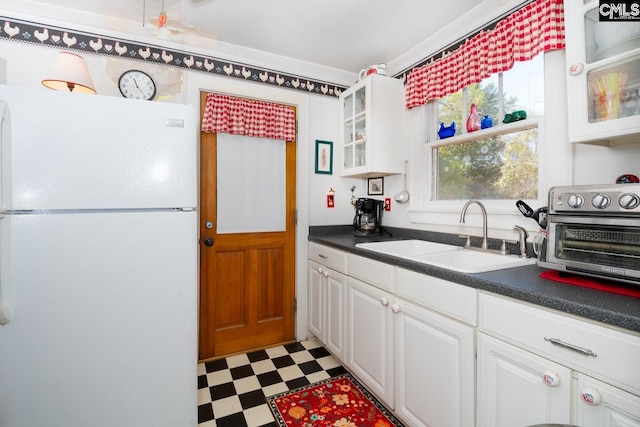 kitchen with light floors, glass insert cabinets, freestanding refrigerator, white cabinetry, and a sink