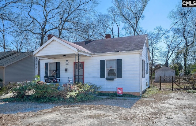 bungalow-style home featuring covered porch, a chimney, fence, and roof with shingles