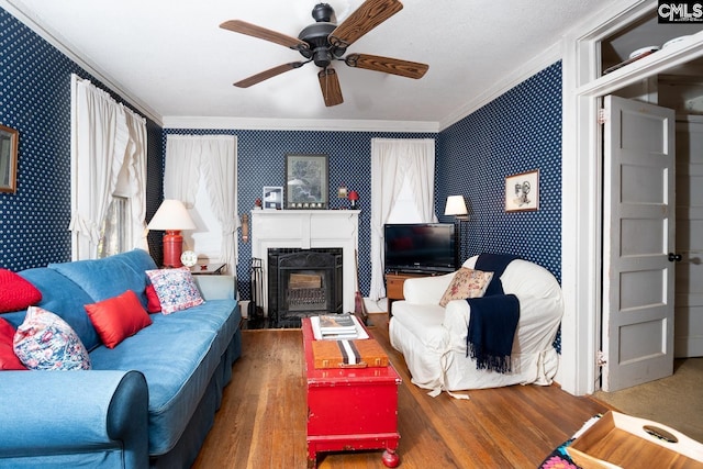 living area with ornamental molding, wood finished floors, a fireplace with flush hearth, and wallpapered walls