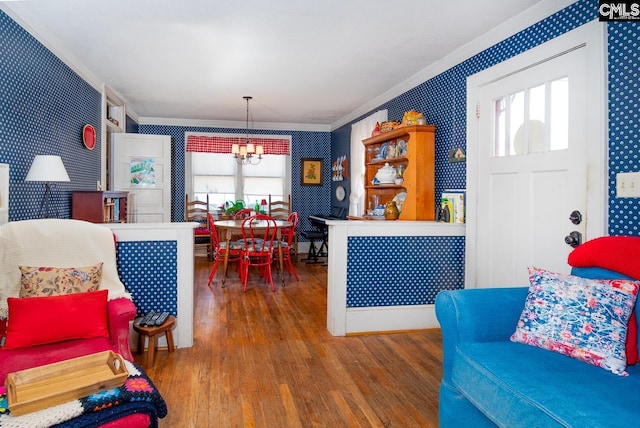 living room with wood finished floors, crown molding, an inviting chandelier, and wallpapered walls