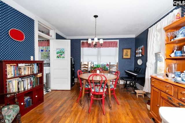 dining room with crown molding, an inviting chandelier, wood finished floors, and wallpapered walls