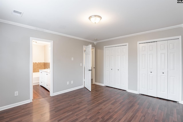 unfurnished bedroom with visible vents, dark wood finished floors, baseboards, and two closets