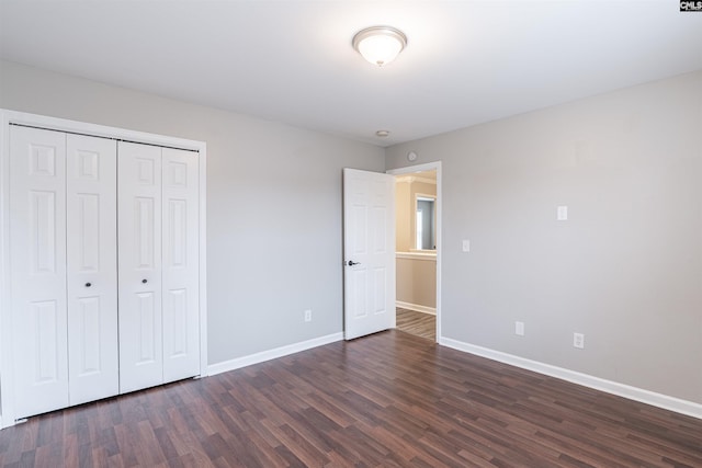 unfurnished bedroom with a closet, baseboards, and dark wood-type flooring