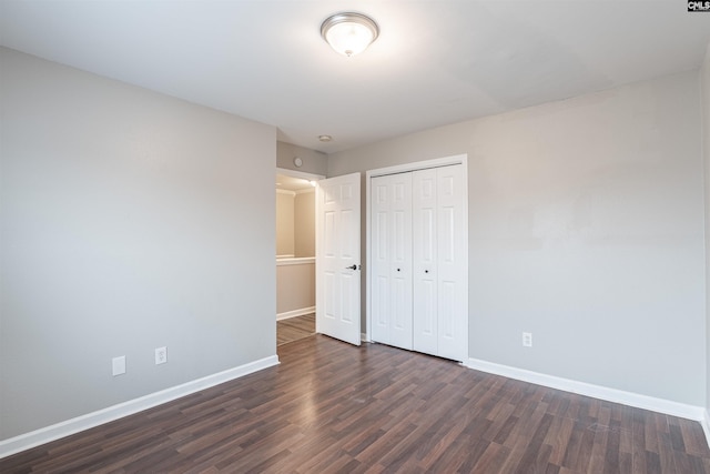 unfurnished bedroom with a closet, baseboards, and dark wood-style flooring