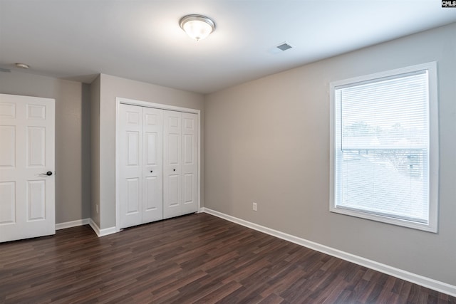 unfurnished bedroom featuring a closet, visible vents, dark wood finished floors, and baseboards