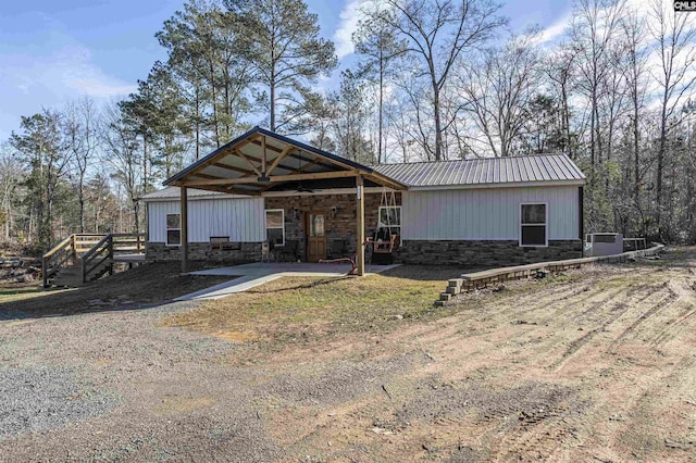 exterior space featuring stone siding, metal roof, and dirt driveway