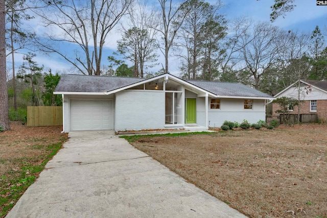 mid-century inspired home with brick siding, roof with shingles, concrete driveway, fence, and a garage