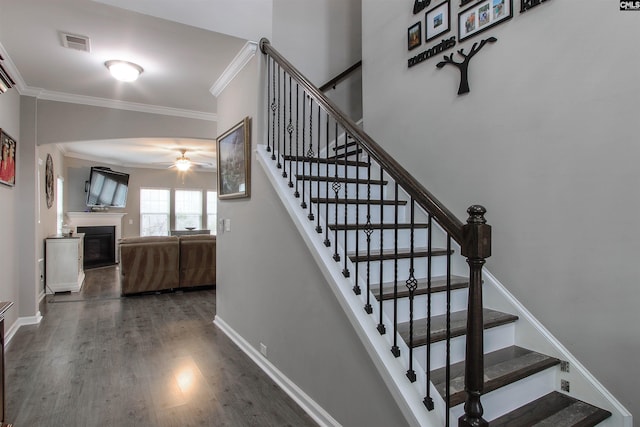 stairway featuring a fireplace, visible vents, ornamental molding, wood finished floors, and baseboards