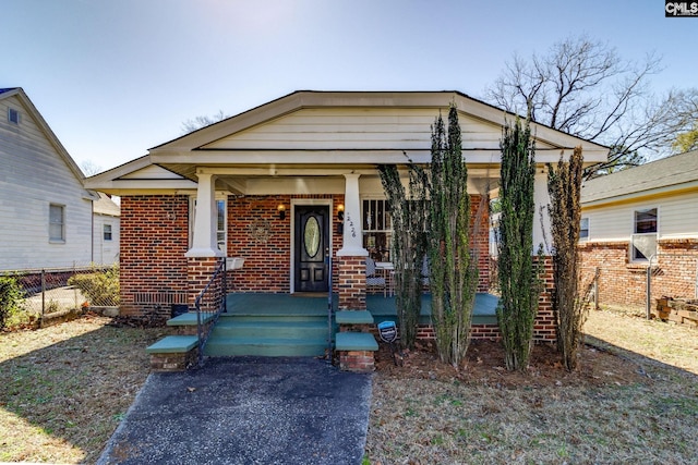 view of front facade featuring covered porch, fence, and brick siding