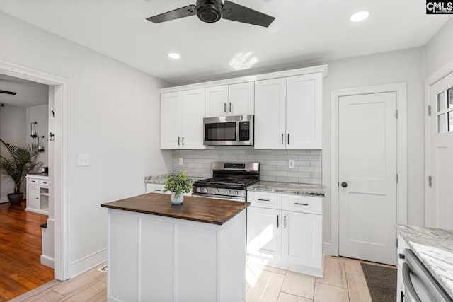 kitchen featuring stainless steel appliances, white cabinets, a kitchen island, and wooden counters