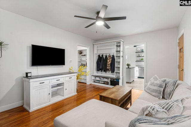 living room with light wood-type flooring, ceiling fan, built in features, and baseboards