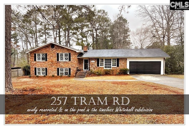 tri-level home with a garage, brick siding, fence, driveway, and a chimney