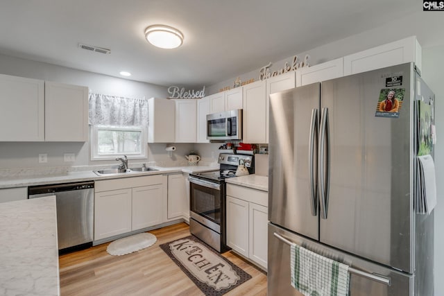 kitchen with a sink, visible vents, light wood-style floors, white cabinets, and appliances with stainless steel finishes