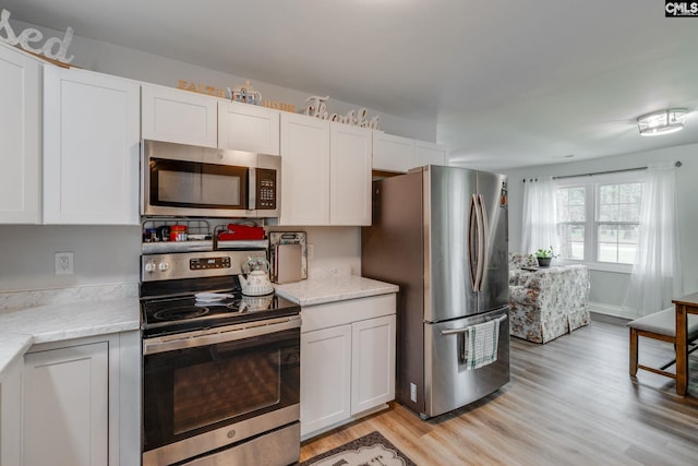 kitchen with white cabinets, light stone countertops, light wood-style flooring, and stainless steel appliances