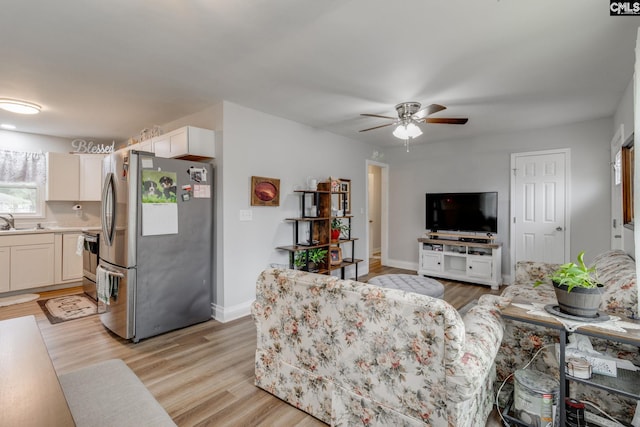 living area with baseboards, ceiling fan, and light wood finished floors