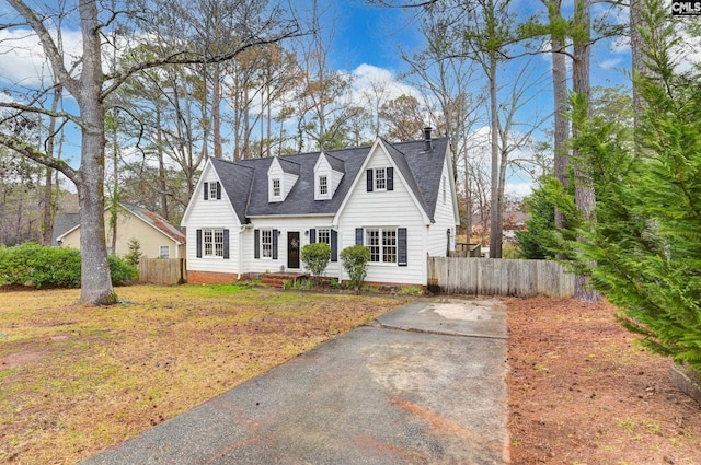 cape cod house with roof with shingles, a chimney, and fence