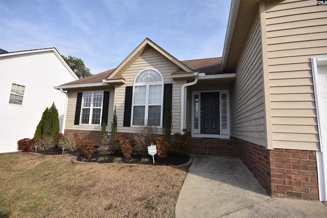 view of exterior entry with a shingled roof, brick siding, and a lawn